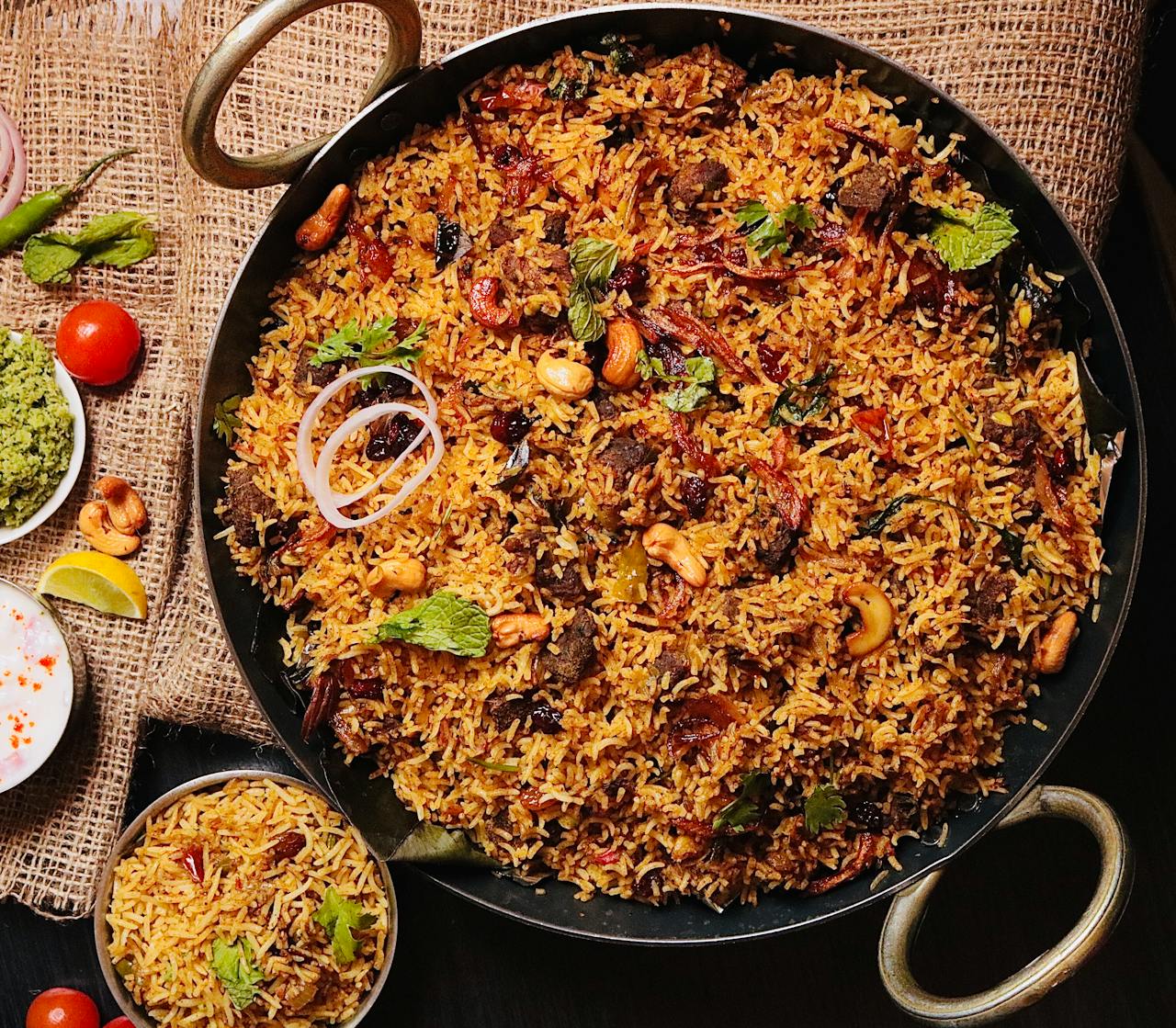 Top view of flavorful Indian biryani in a cooking pan, garnished with cashews and herbs.